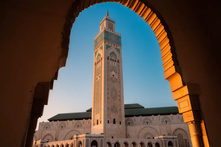 The minaret of the Hassan II Mosque in Casablanca at dusk, framed by a carved archway