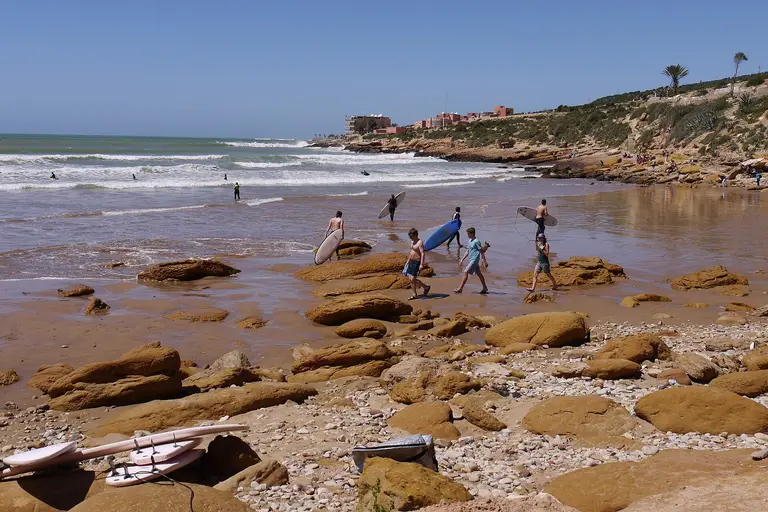 Surfers walking into the waves on the rocky beach at Taghazout